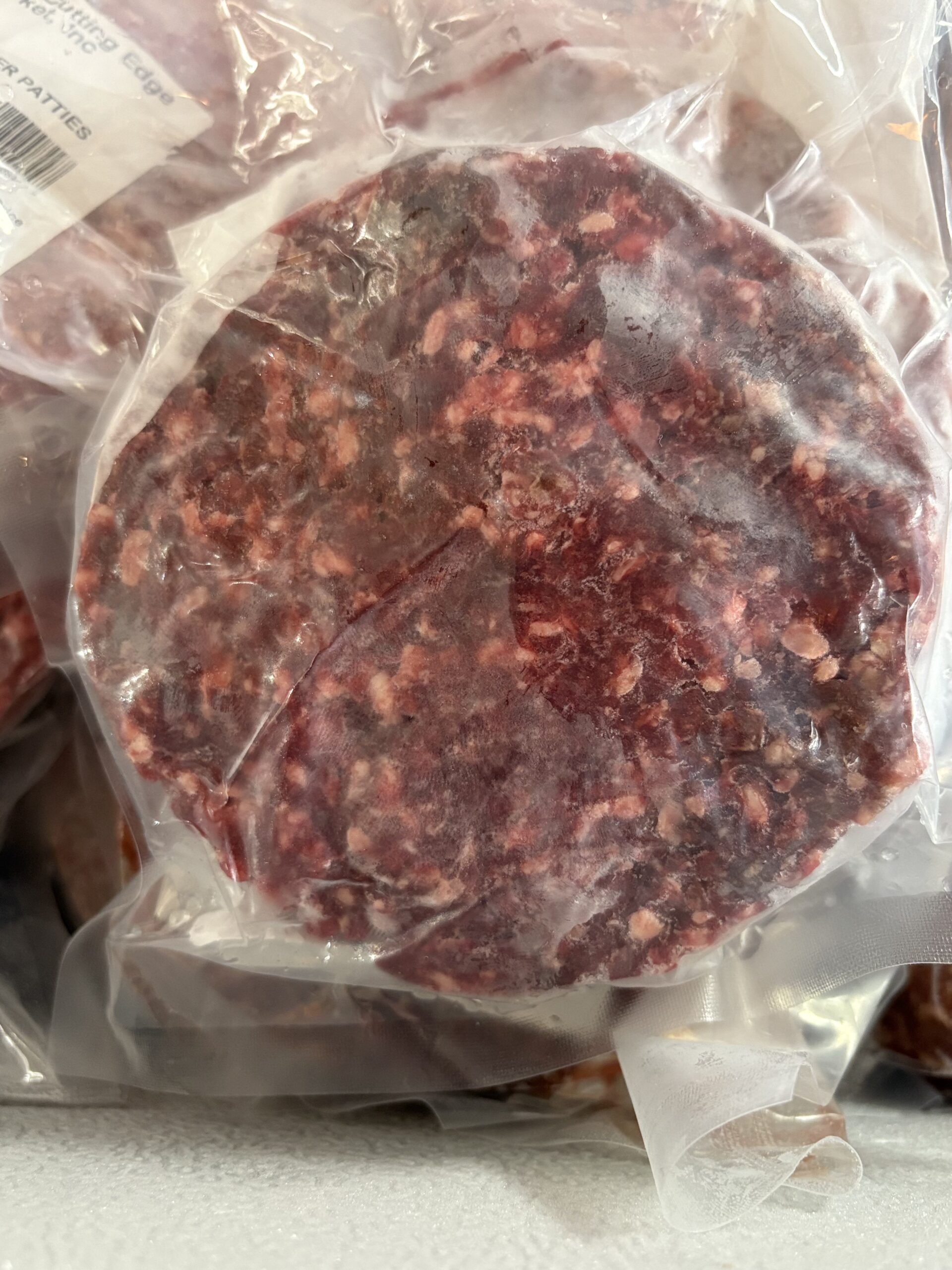 Vacuum-sealed beef patties displayed in packaging, showcasing a rich marbled texture ideal for grilling or cooking.